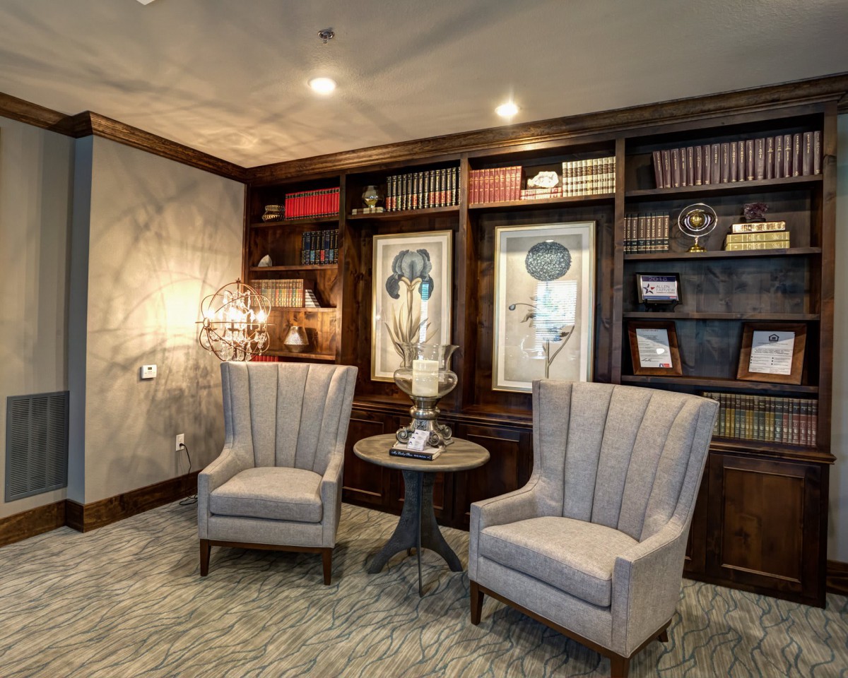 A cozy library corner with two elegant chairs, a small table, and well-stocked bookshelves.
