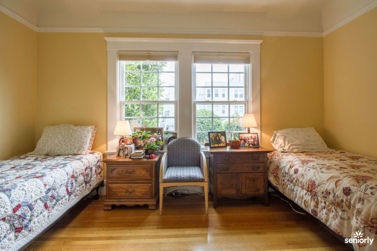 A cozy bedroom with twin beds, warm lighting, and large windows.