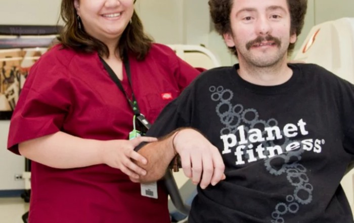 Two people smiling indoors, with one wearing a Planet Fitness shirt.