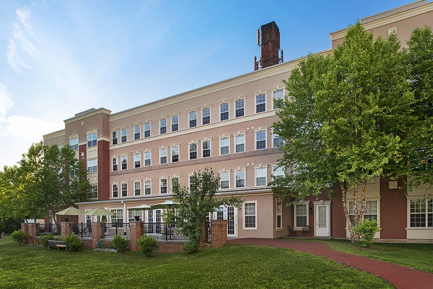 A multi-story residential building with brick and siding, featuring numerous windows and surrounded by trees and a well-kept lawn.