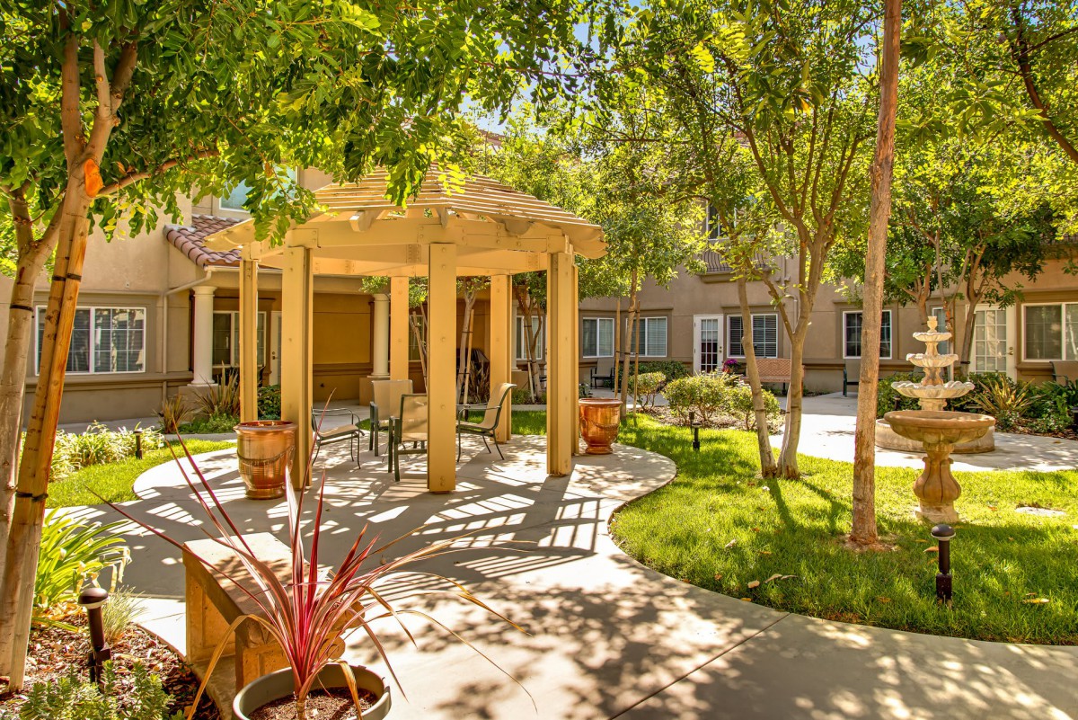 A serene courtyard featuring a pergola, lush trees, and a landscaped walkway.