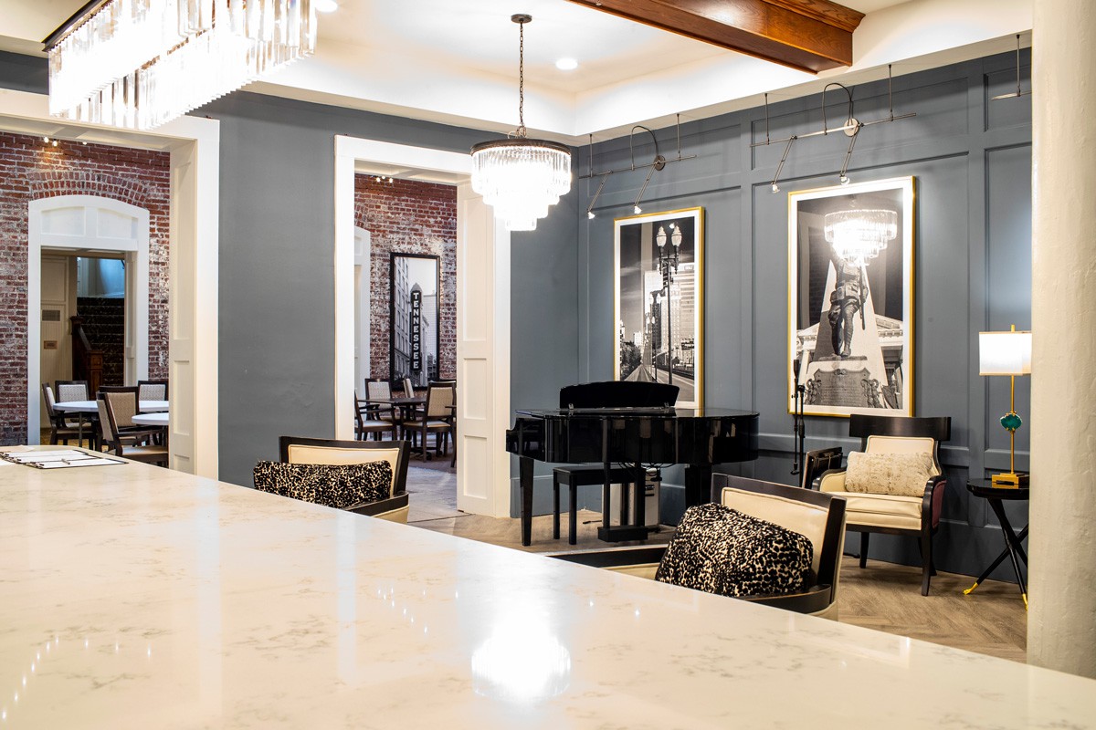 A stylish and elegant living room featuring a grand piano, modern artwork, and a chandelier.