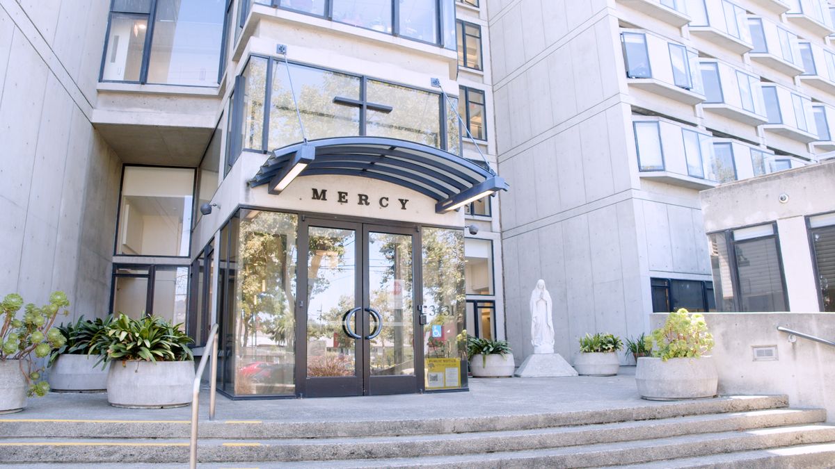 The entrance of a modern building with glass doors and a statue nearby.