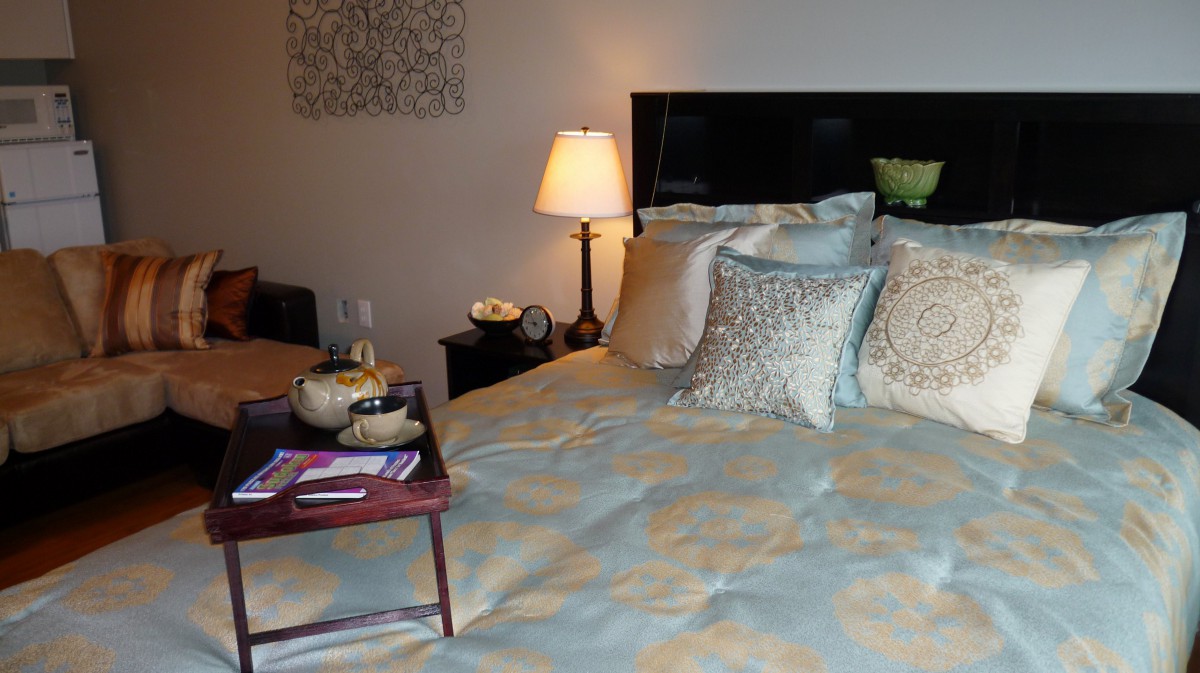 A cozy bedroom with elegant bedding and a bedside lamp, featuring decorative pillows and a serving tray.