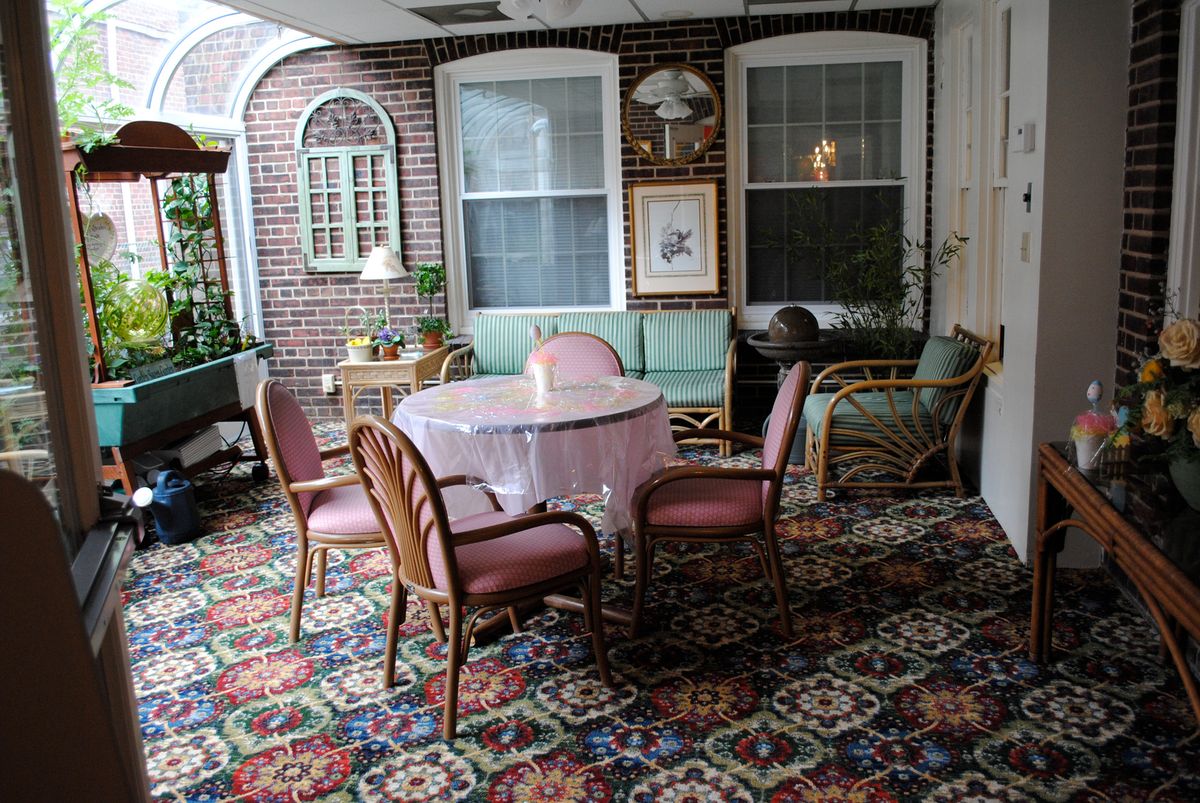 A cozy seating area with a table and chairs, featuring a decorative carpet and large windows.