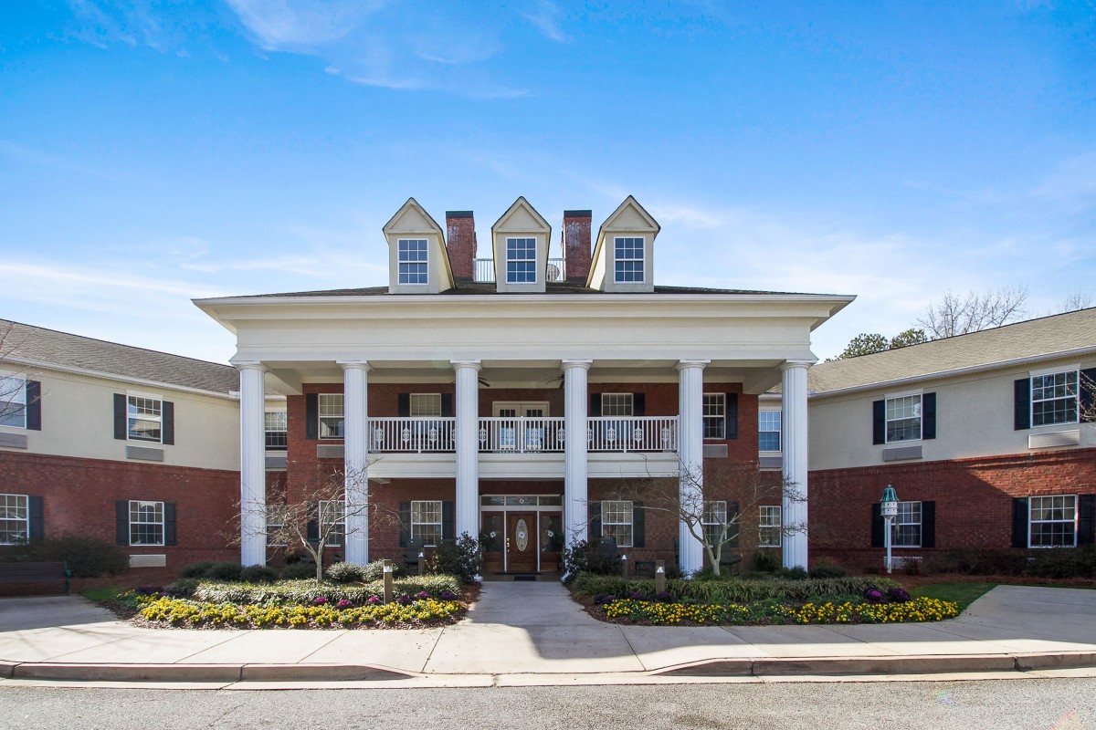 A two-story residential building with prominent columns and brick exterior under a clear blue sky.