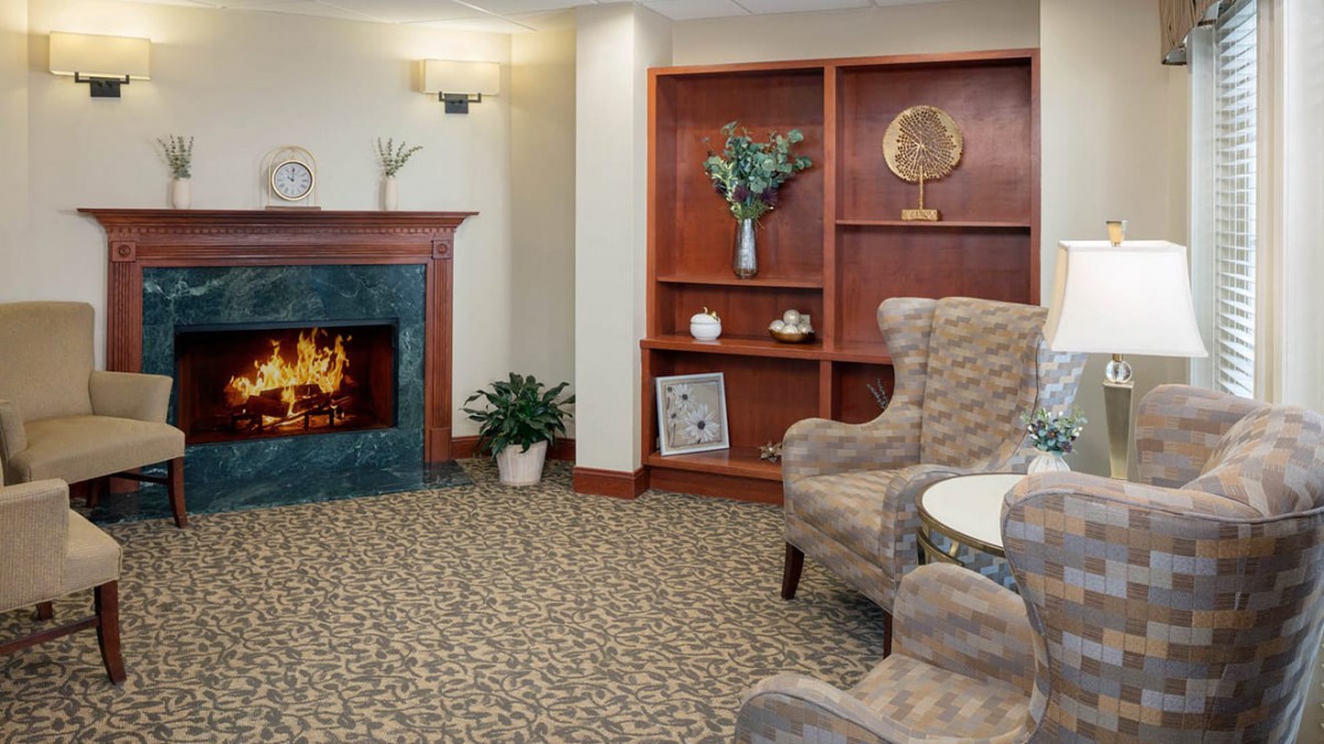 A cozy living room featuring a fireplace, armchairs, and a bookshelf with decorative items.