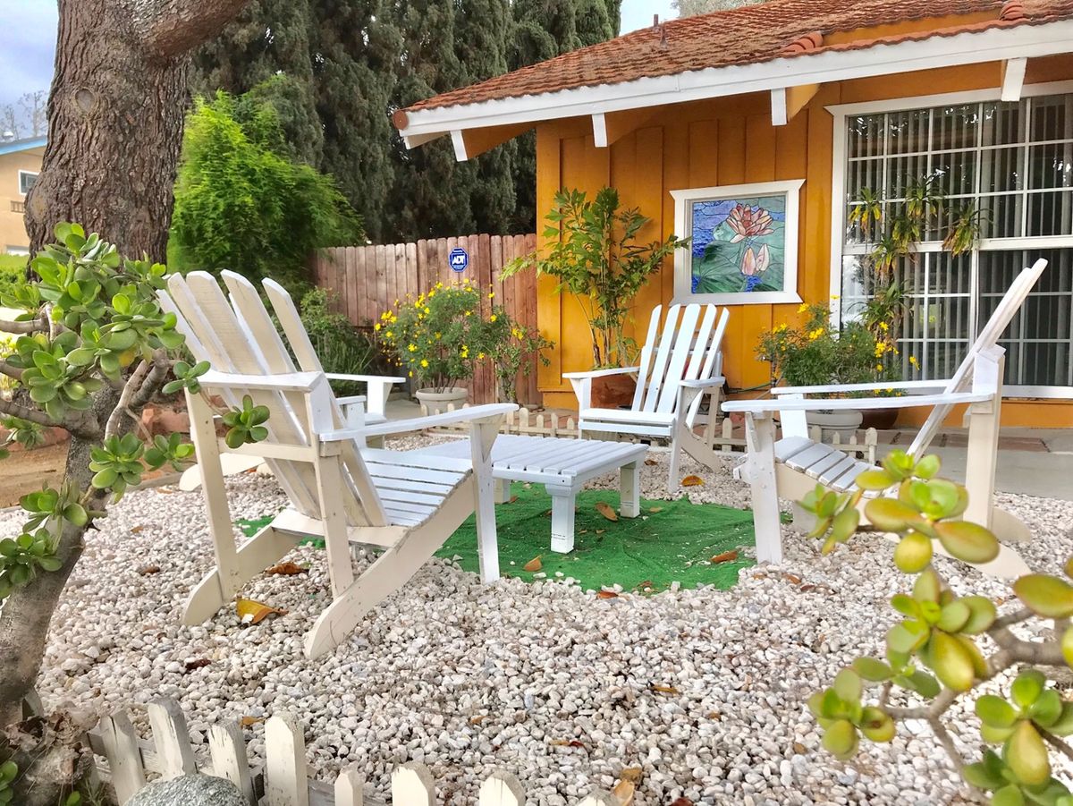 A cozy outdoor patio area with white wooden chairs and a small garden in front of a house.