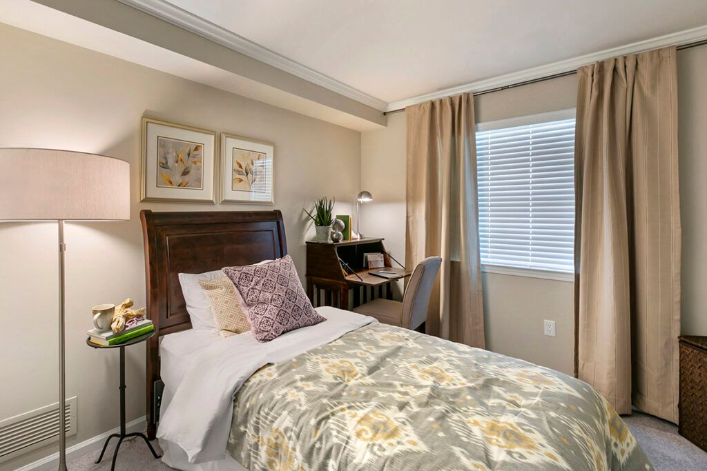 A cozy bedroom with a single bed, a small desk, and decorative pillows.