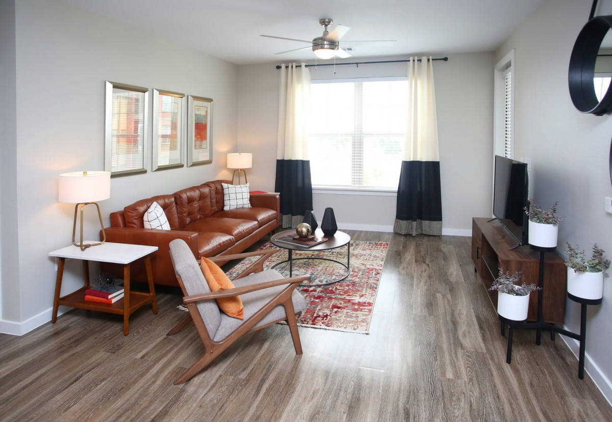 A cozy living room featuring mid-century modern furniture, including a leather sofa and armchairs, with wood flooring and ample natural light.