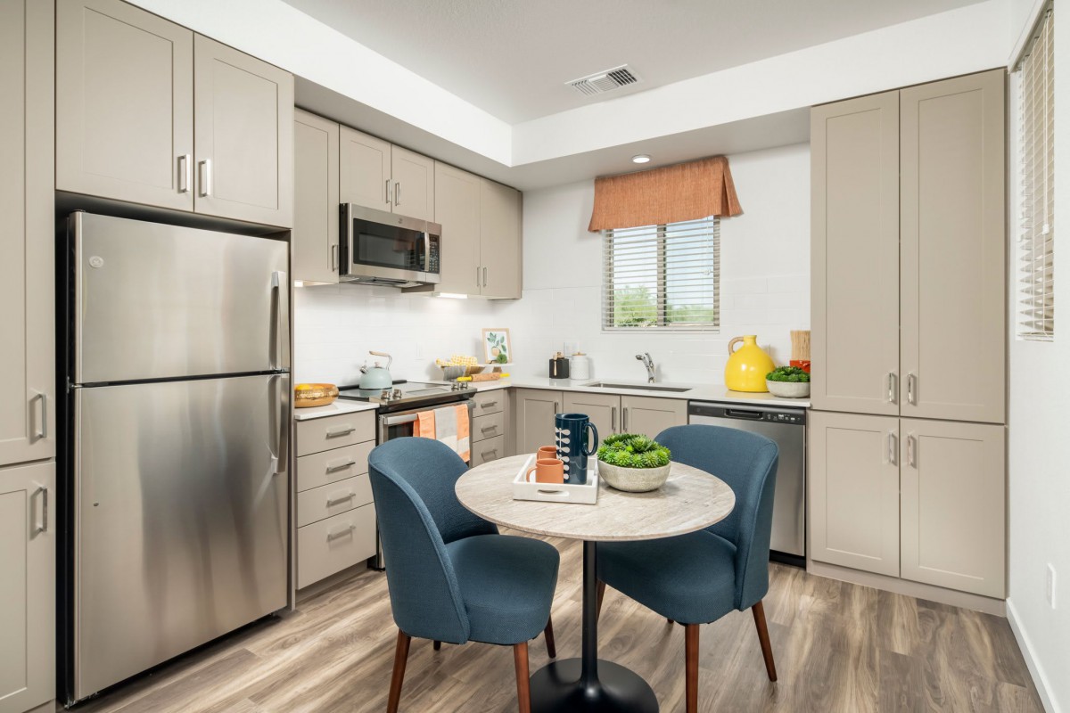 A modern kitchen with sleek appliances and stylish furniture, featuring a dining table with blue chairs.