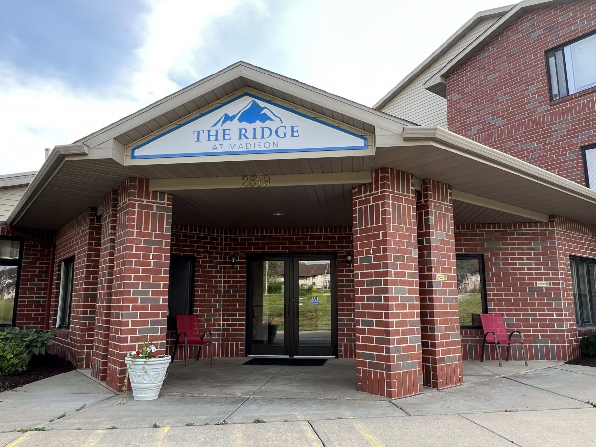 Entrance of a brick building with an awning and two chairs.