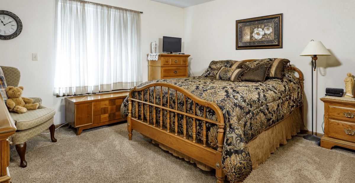 A cozy bedroom featuring a wooden bedframe with patterned bedding, a dresser with a television on top, and decorative elements.
