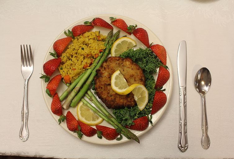 A beautifully arranged meal featuring a fried patty, asparagus, lemon slices, rice, and strawberries.