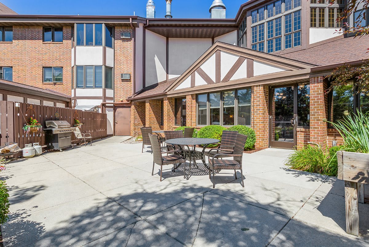 A sunny outdoor patio area with tables and chairs in front of a brick building.