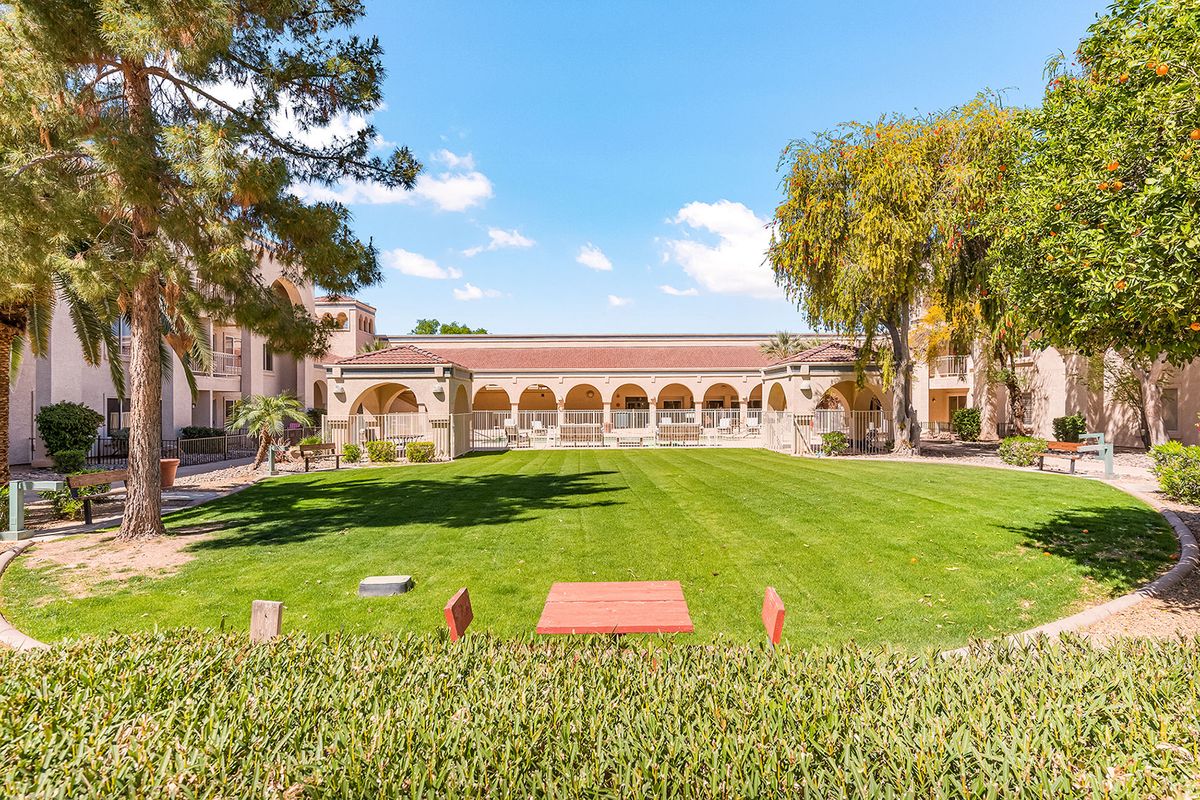 A sunny day in a courtyard with green lawns, surrounded by arched architecture and trees.