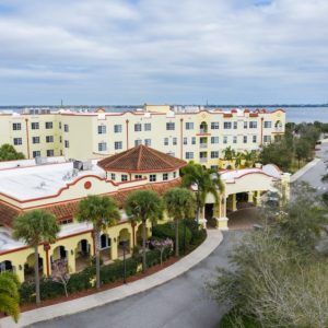 A scenic view of a resort building surrounded by palm trees with a body of water in the background.