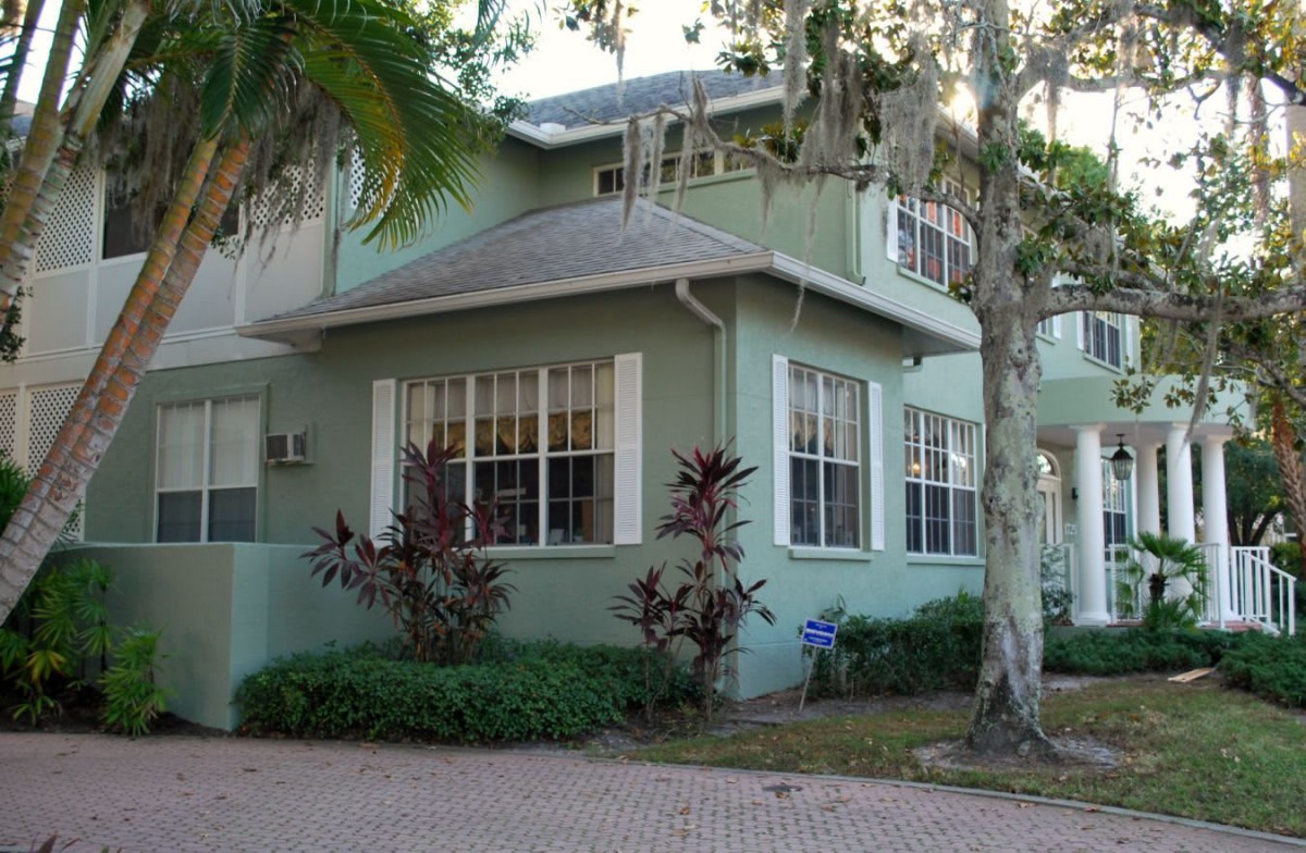 A green residential house surrounded by trees and landscaping.