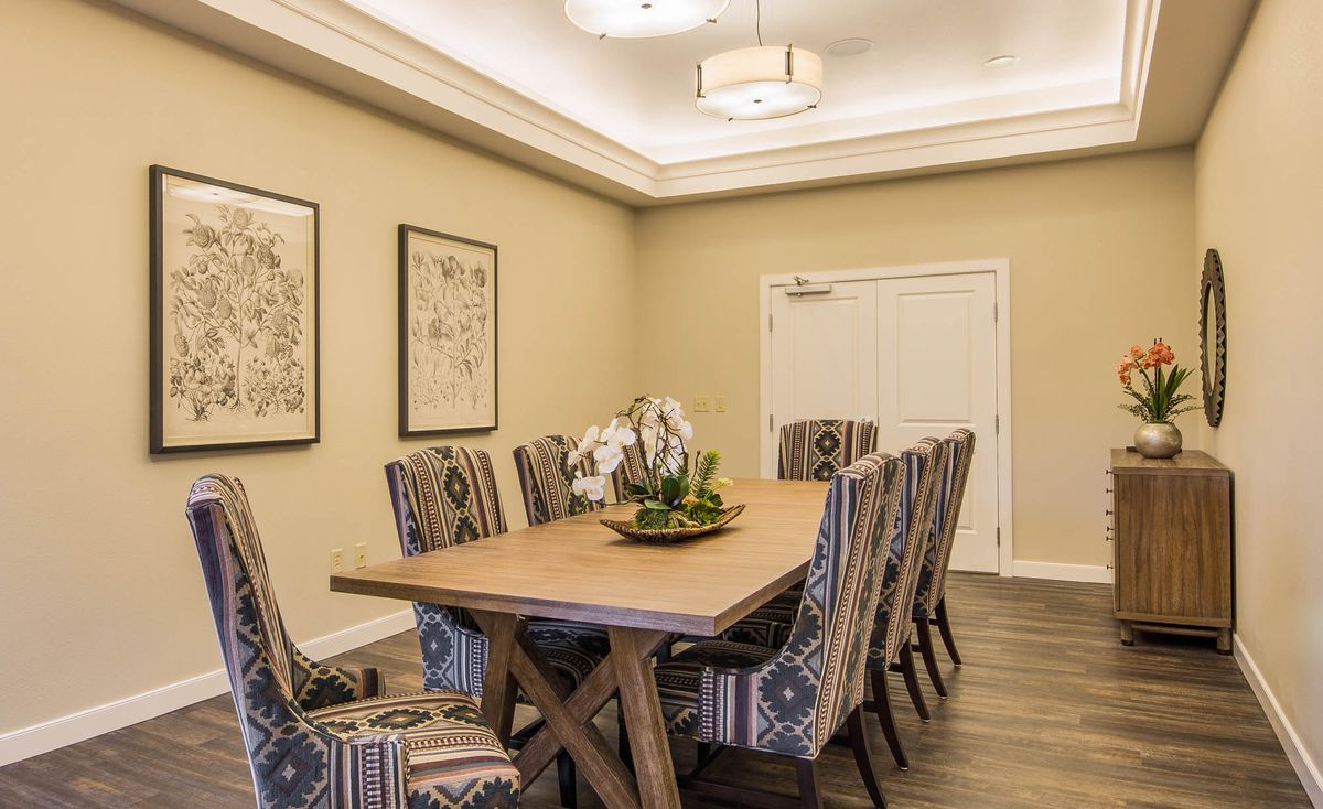 A modern dining room with a wooden table and patterned chairs, featuring elegant lighting and framed artwork on the walls.