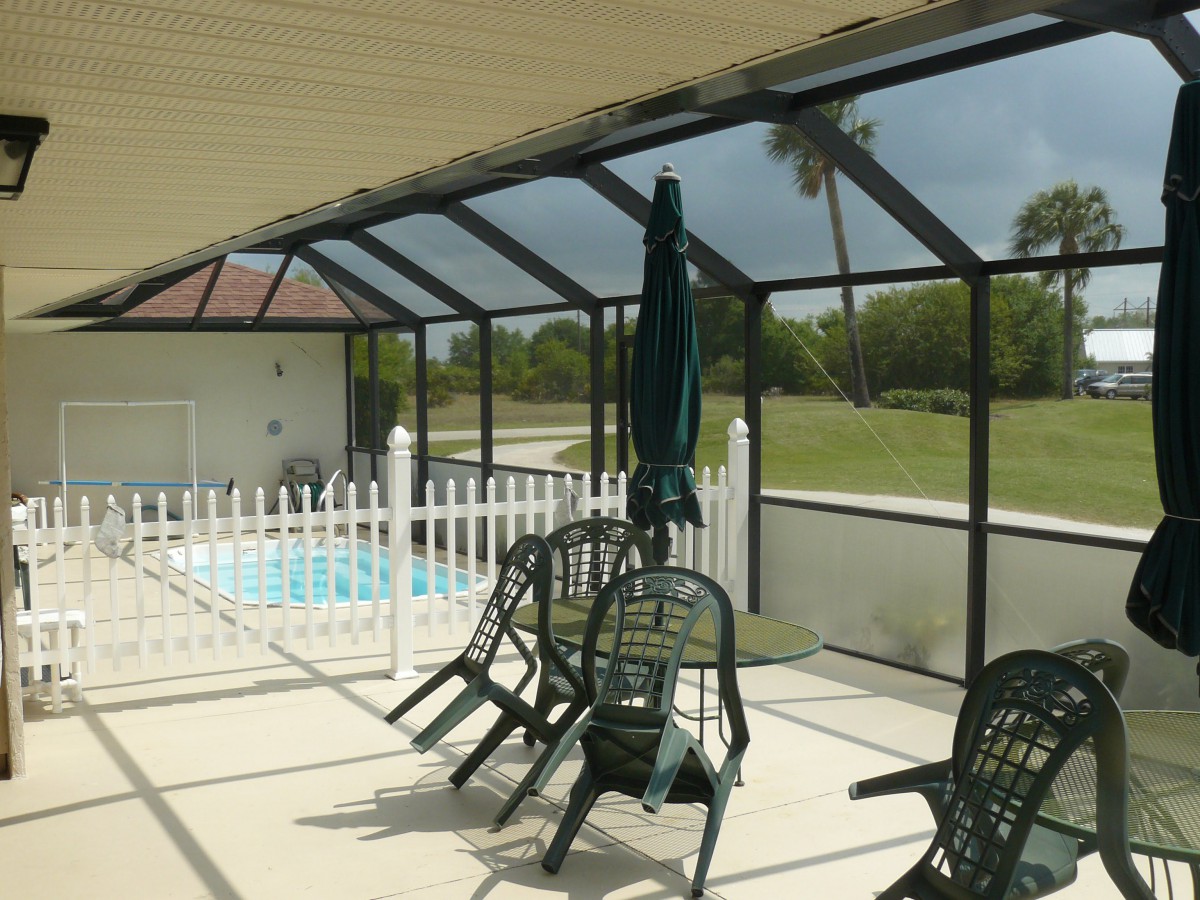 A screened-in patio with poolside furniture and a view of the outdoors.