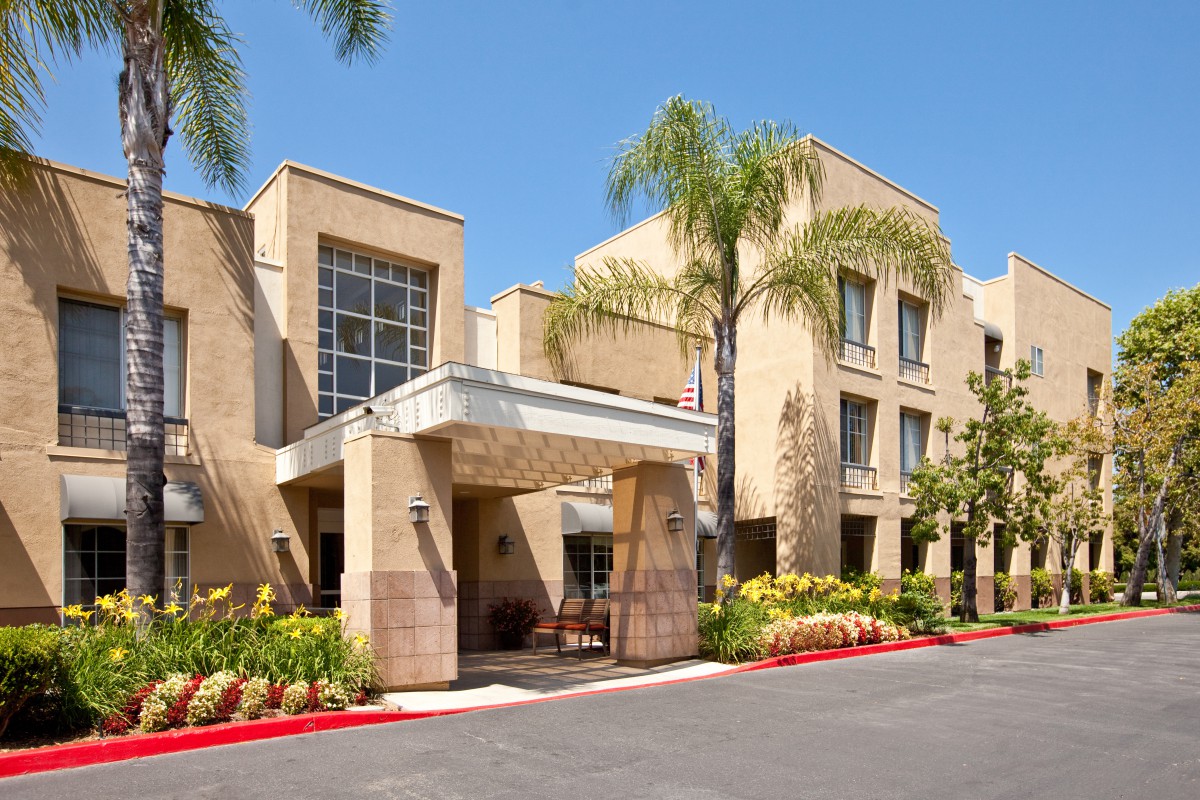 A modern hotel entrance surrounded by palm trees and landscaped gardens.