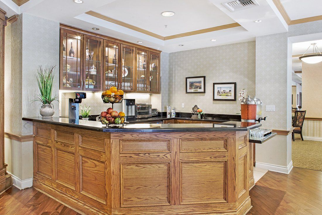 A cozy kitchen bar area with wooden cabinetry and a granite countertop, featuring appliances and fruit arrangements.