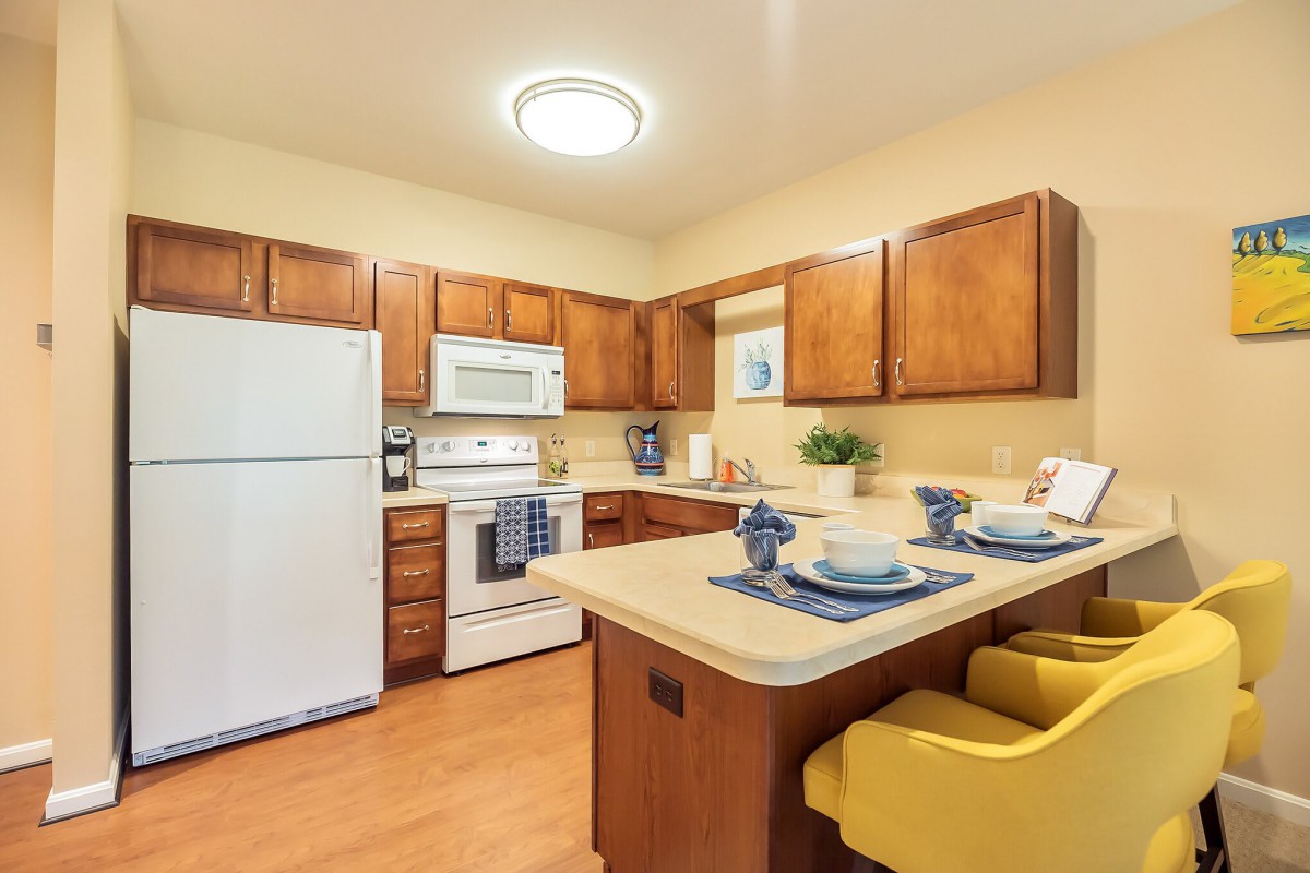 A modern kitchen with wooden cabinets, equipped with appliances and a small dining area.