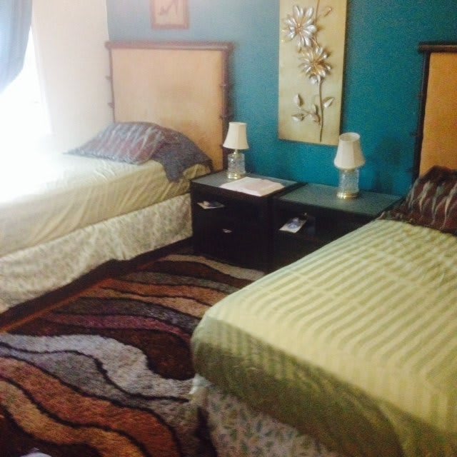 A cozy bedroom with twin beds, a shared nightstand, decorative lamps, and a colorful rug.