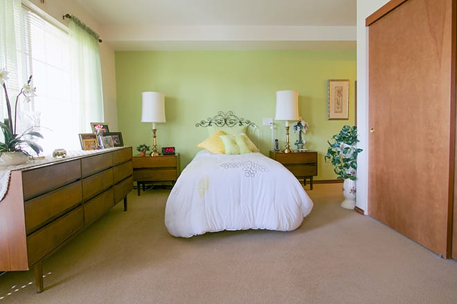 A cozy bedroom with vintage decor featuring a double bed, green walls, and mid-century furniture.