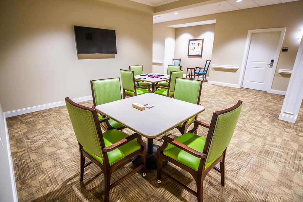 A brightly lit dining or meeting area with green chairs and a television.