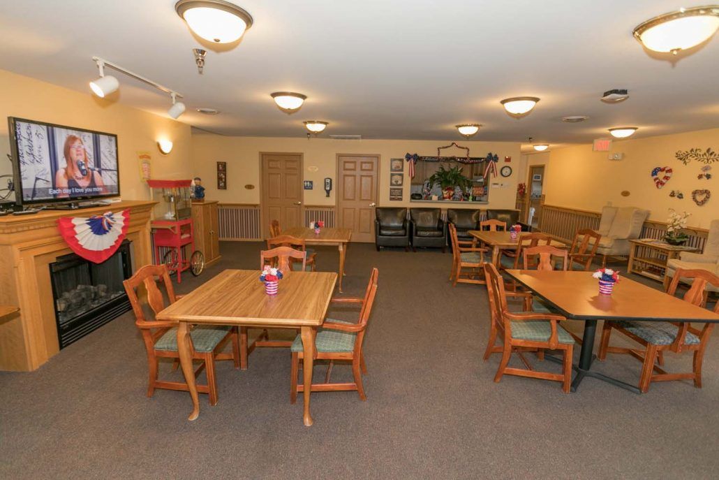 A cozy dining area with wooden tables and chairs, softly lit by ceiling lights.