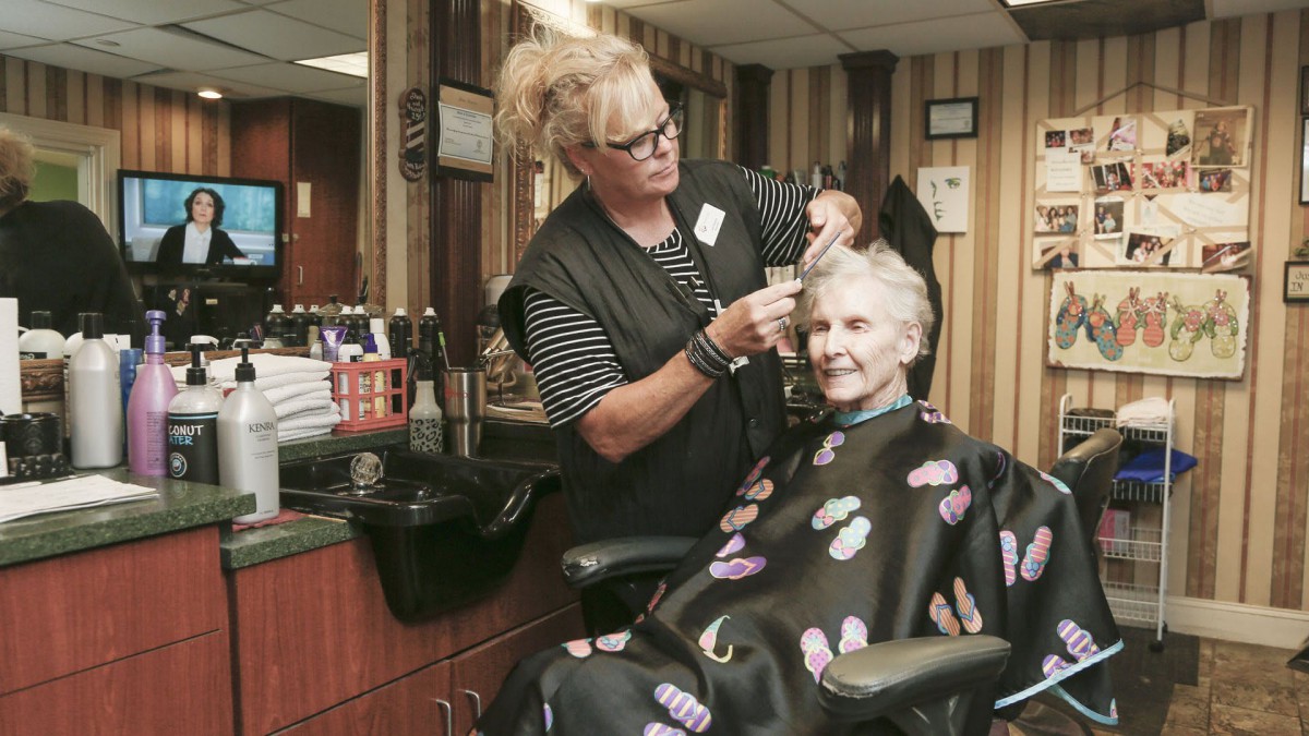 An elderly woman getting her hair styled by a hairdresser at a salon, both smiling.