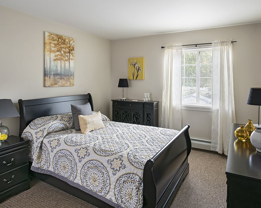 A cozy bedroom with a large bed, dresser, and window letting in natural light.