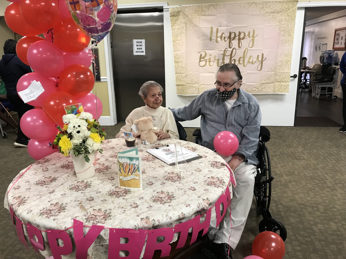 Two people celebrating a birthday with balloons, flowers, and a decorated table.