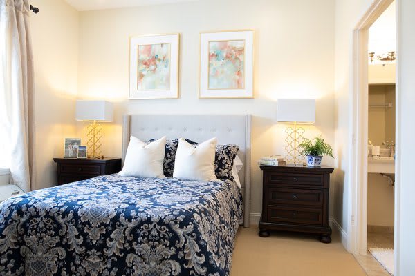 A well-decorated bedroom featuring a bed with a patterned comforter, two nightstands with lamps, and framed artwork above the headboard.