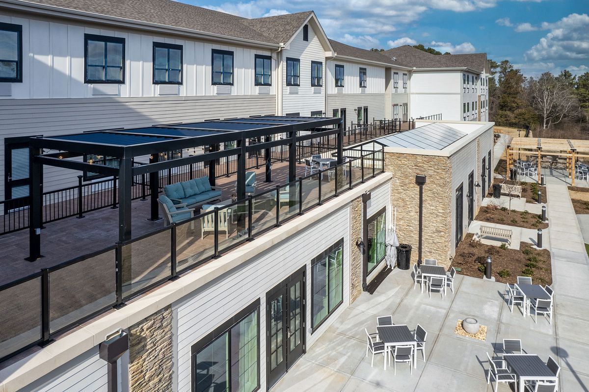 A modern residential building with outdoor seating and a glass-railed patio.