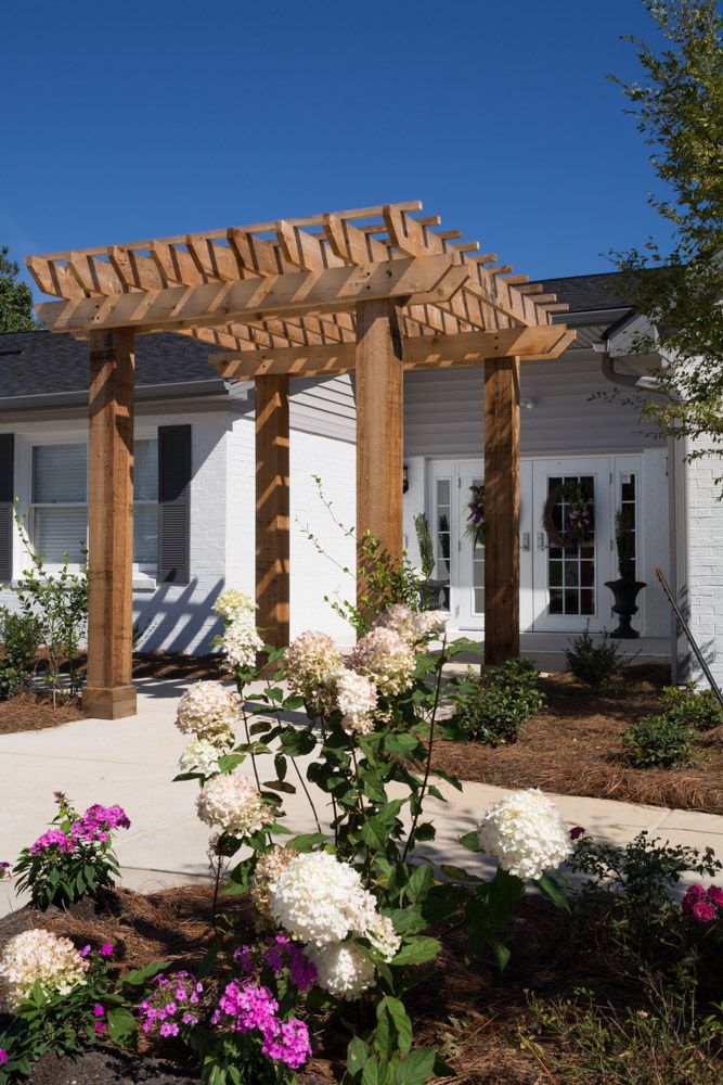 A beautifully landscaped garden with a wooden pergola in front of a house.