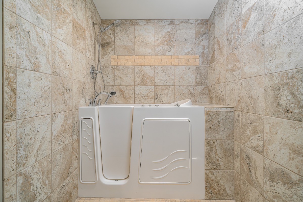 A bathroom featuring a walk-in bathtub with tiled walls, designed for accessibility and comfort.