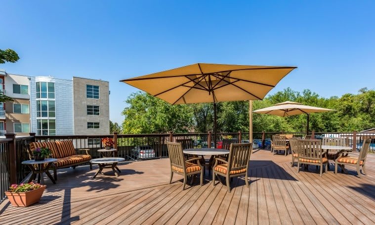 A sunny outdoor patio area with tables, chairs, and large umbrellas on a wooden deck.