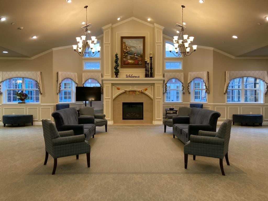 A spacious and elegant living room with a symmetrical arrangement of armchairs, featuring a central fireplace and large arched windows.
