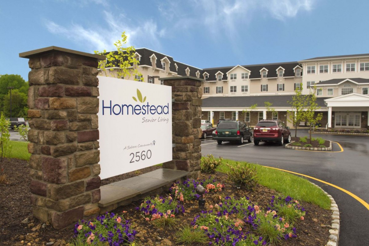 Exterior view of Homestead Suites, featuring a sign and landscaped entrance.