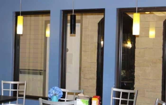 A small seating area with a table and chairs, set against a blue wall with large windows.
