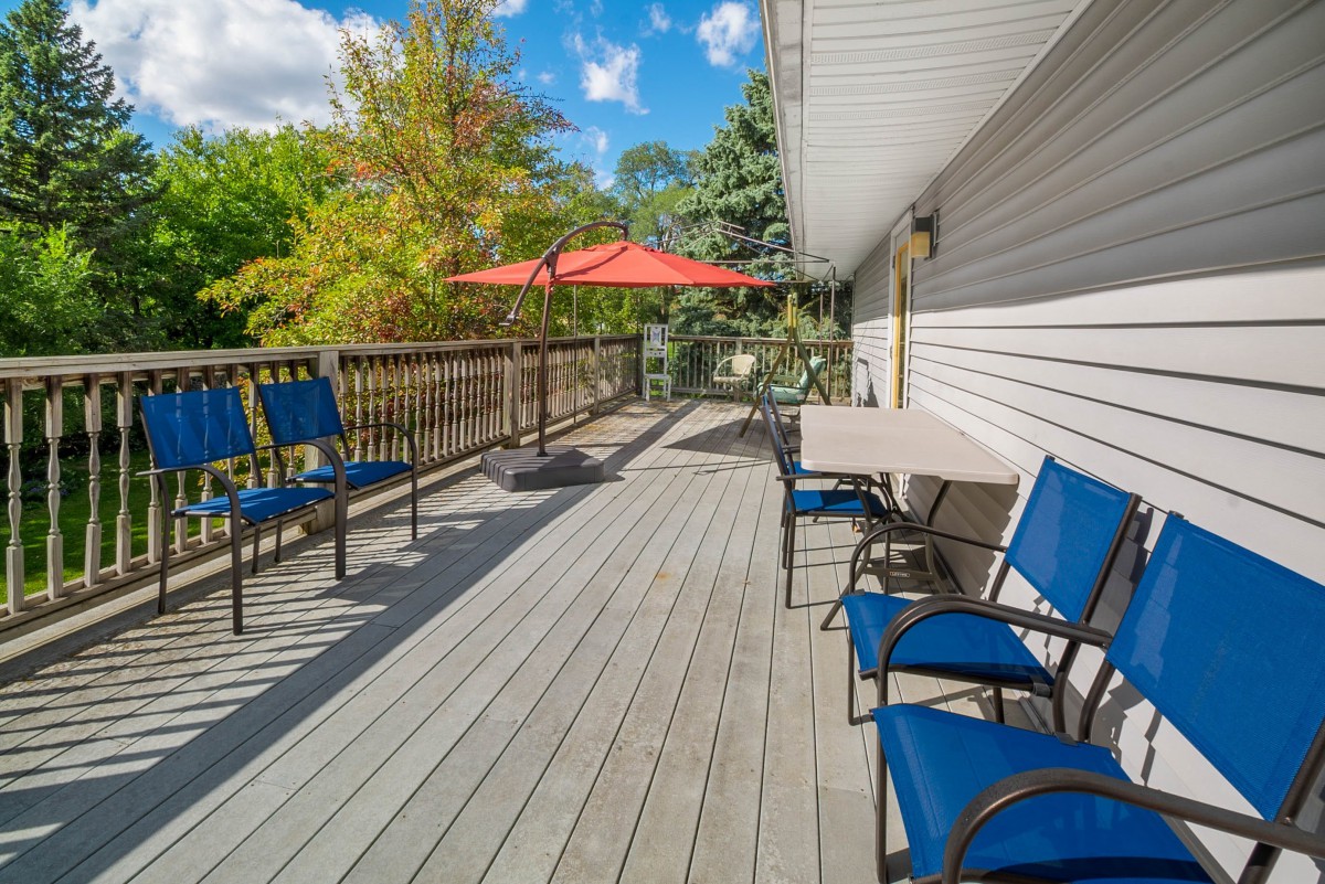 A sunny outdoor deck with blue chairs and a table under a red umbrella.