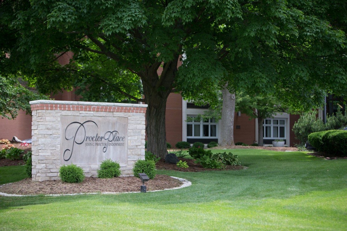 A scenic view of a college campus entrance with a welcoming sign and lush greenery.