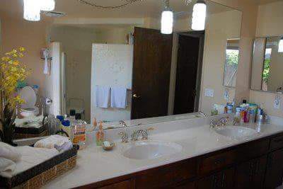 A bathroom with a large mirror, dual sinks, and various items on the countertop.