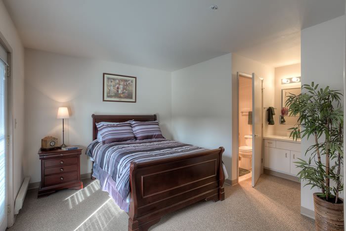 A cozy bedroom with a wooden bed, striped bedding, and an adjoining bathroom.