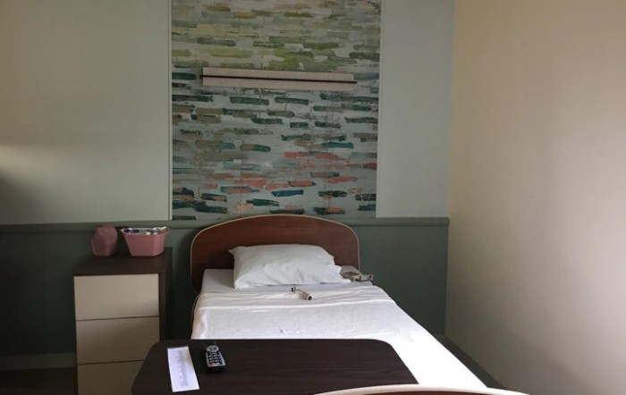 A hospital room with a single bed, pillow, and wall artwork.