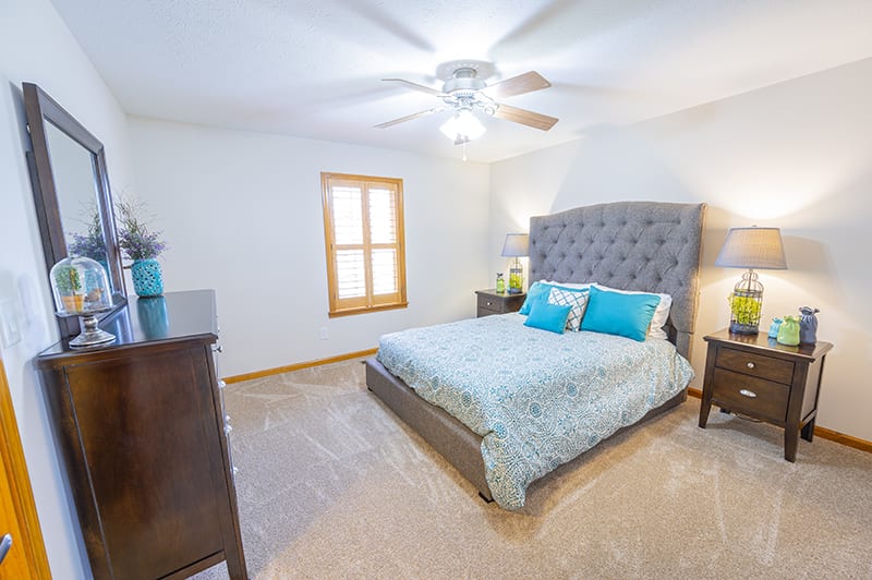 A cozy bedroom with a large bed, carpeted floor, and ceiling fan.