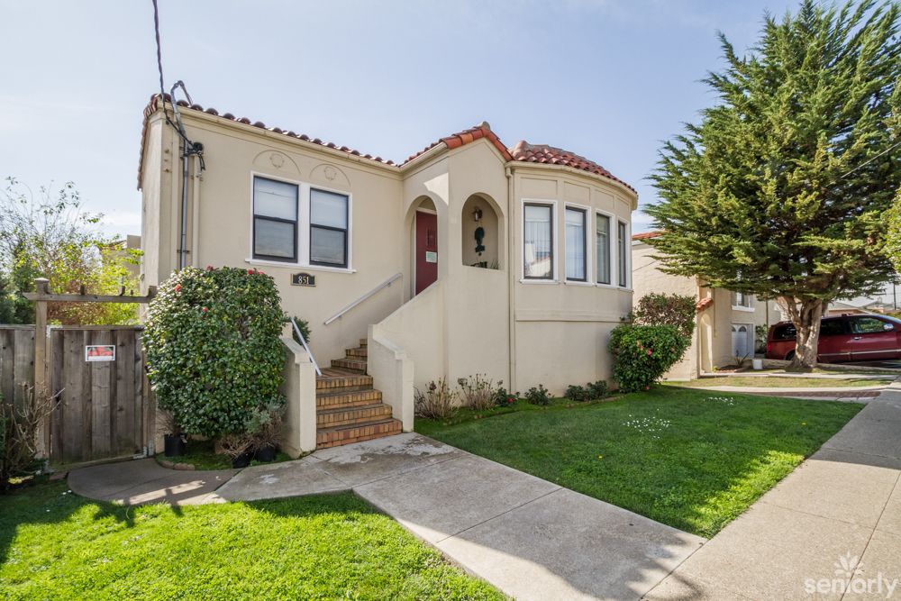 A quaint stucco house with a manicured front yard and steps leading to the entrance.