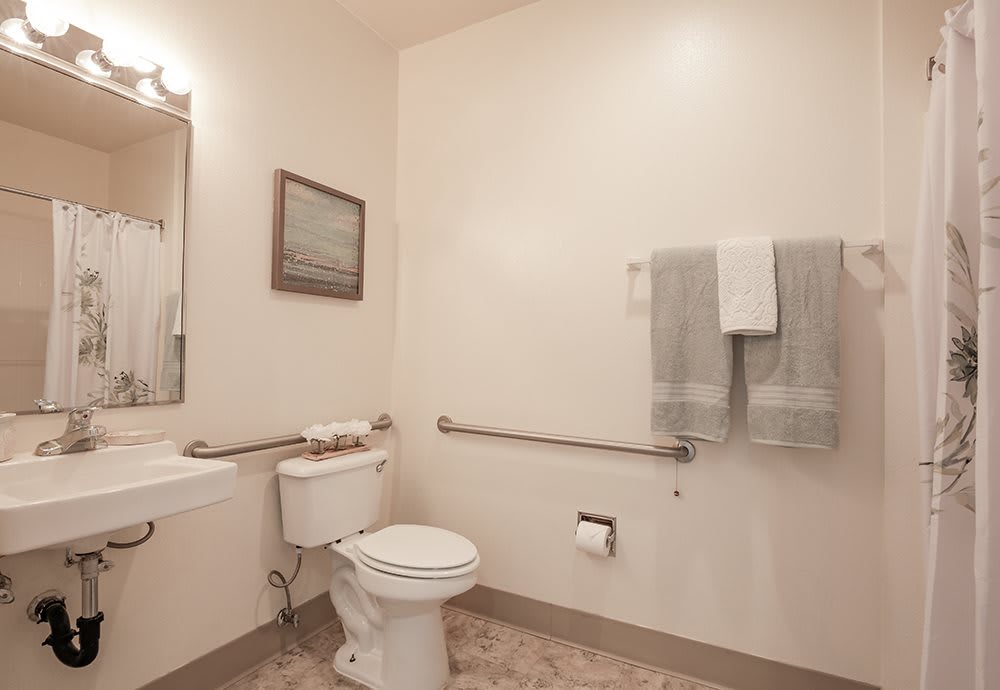 A clean and accessible bathroom with a toilet, sink, mirror, and towels.